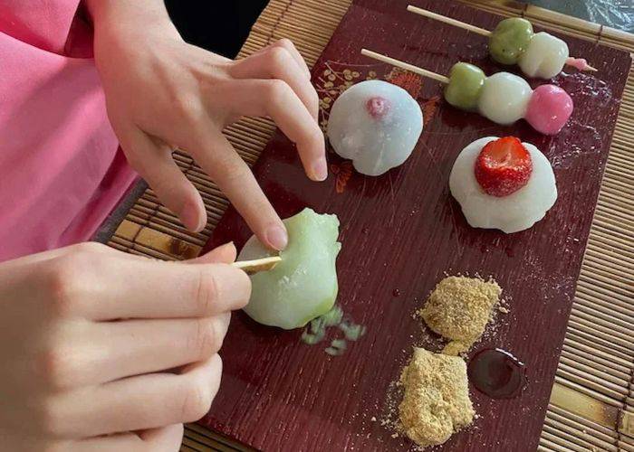 A serving tray of assorted Japanese wagashi. A guest is using a tool to shape another sweet.
